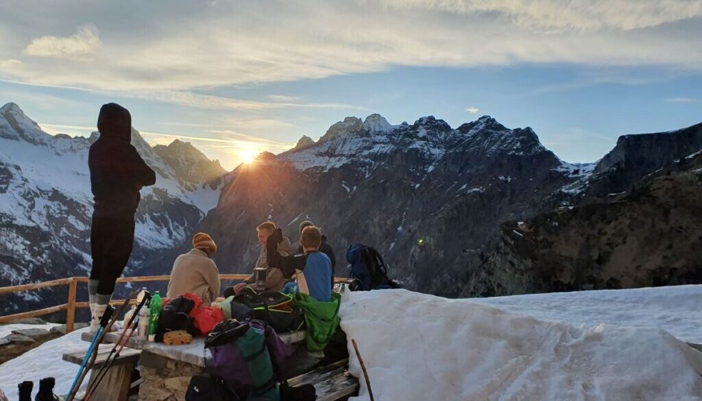 a group of friends watching the sun setting behind the snowy mountains on the other side of the verzasca valley, at the Capanna Cognóra in Ticino, Switzerland