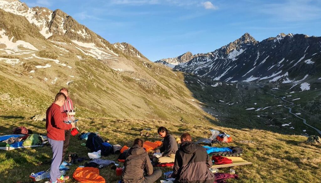 a group of friends preparing dinner during the sunset with scattered camping gear, in grabünden, switzerland