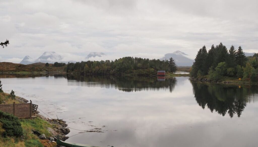 cano in a lake surrounded by pine trees and mountains draped over by clouds in the background on smøla, norway