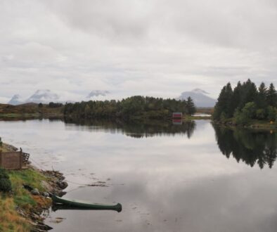 cano in a lake surrounded by pine trees and mountains draped over by clouds in the background on smøla, norway