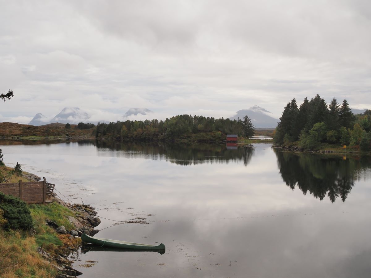 cano in a lake surrounded by pine trees and mountains draped over by clouds in the background on smøla, norway